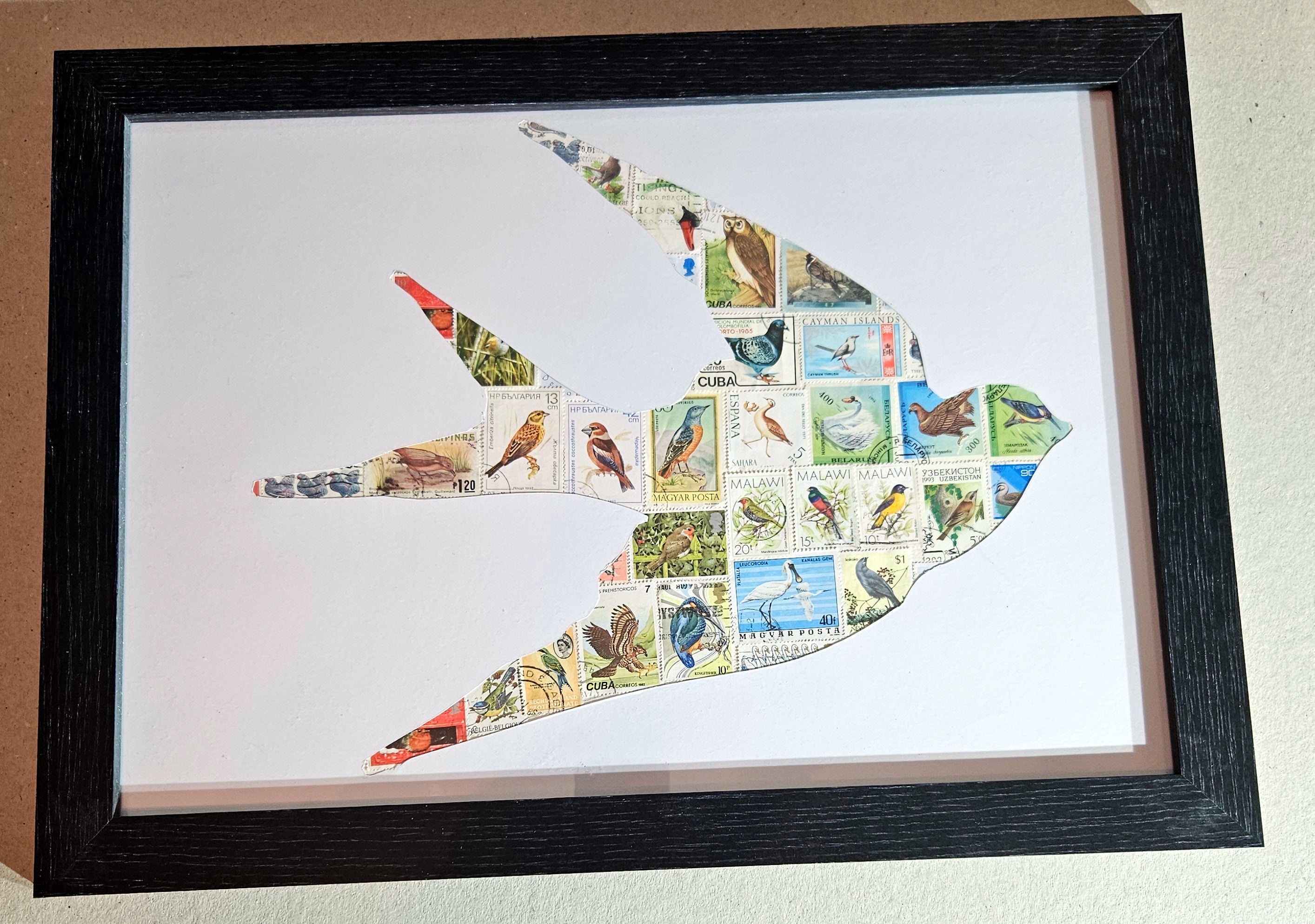 Framed artwork of a bird shape made from various stamps on a white background