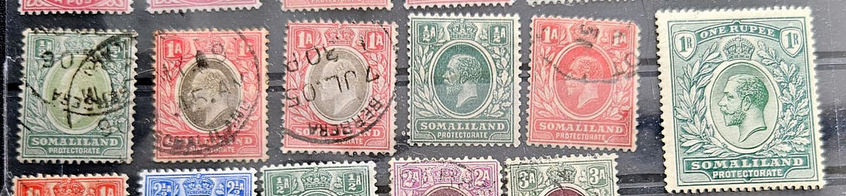 A close-up of several vintage postage stamps from British Somaliland, including red, green, blue, and purple denominations with black cancellation marks, arranged on a dark background.
