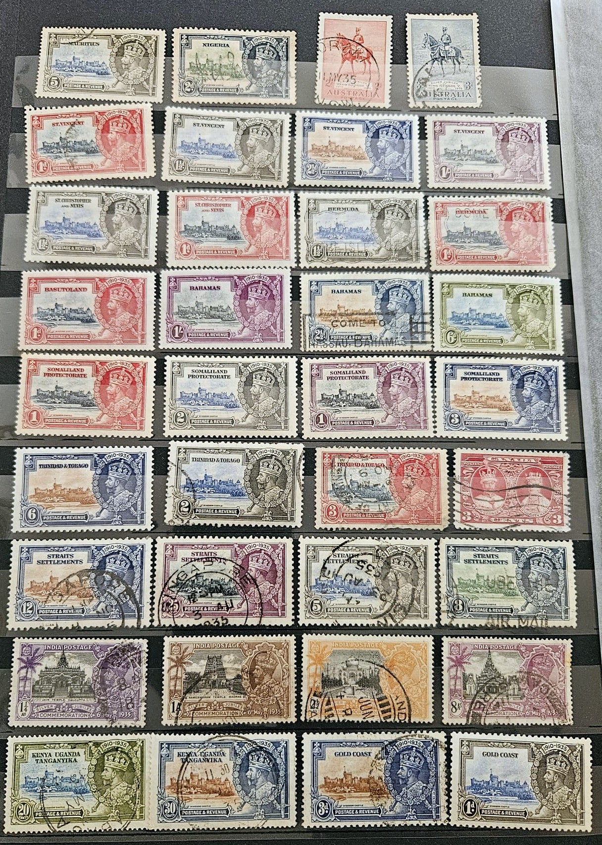 A collection of vintage postage stamps arranged in rows on a dark surface, showing many different colors and designs with cancellation marks.