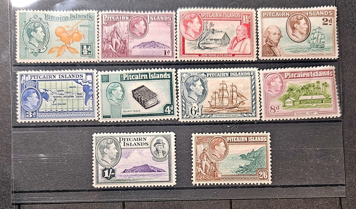 A set of vintage Pitcairn Islands postage stamps arranged on a dark wooden surface. The stamps feature various colors and designs, including portraits of King George V, landscapes, ships, and postal illustrations, with denominations ranging from 1d to 26d.
