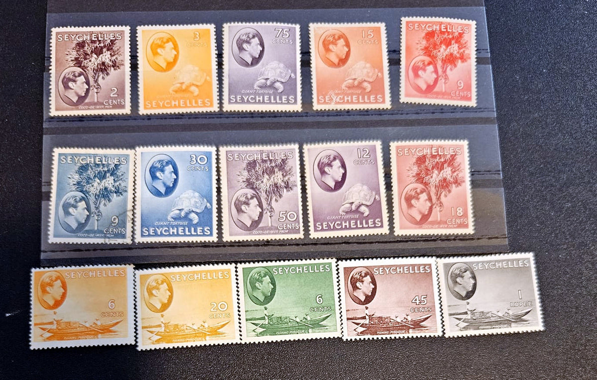A set of vintage Seychelles postage stamps displayed on a black background, arranged in three rows inside a clear plastic protective sleeve. The stamps feature various colors including orange, blue, green, purple, and brown, with designs of a tree, a globe, and boats.