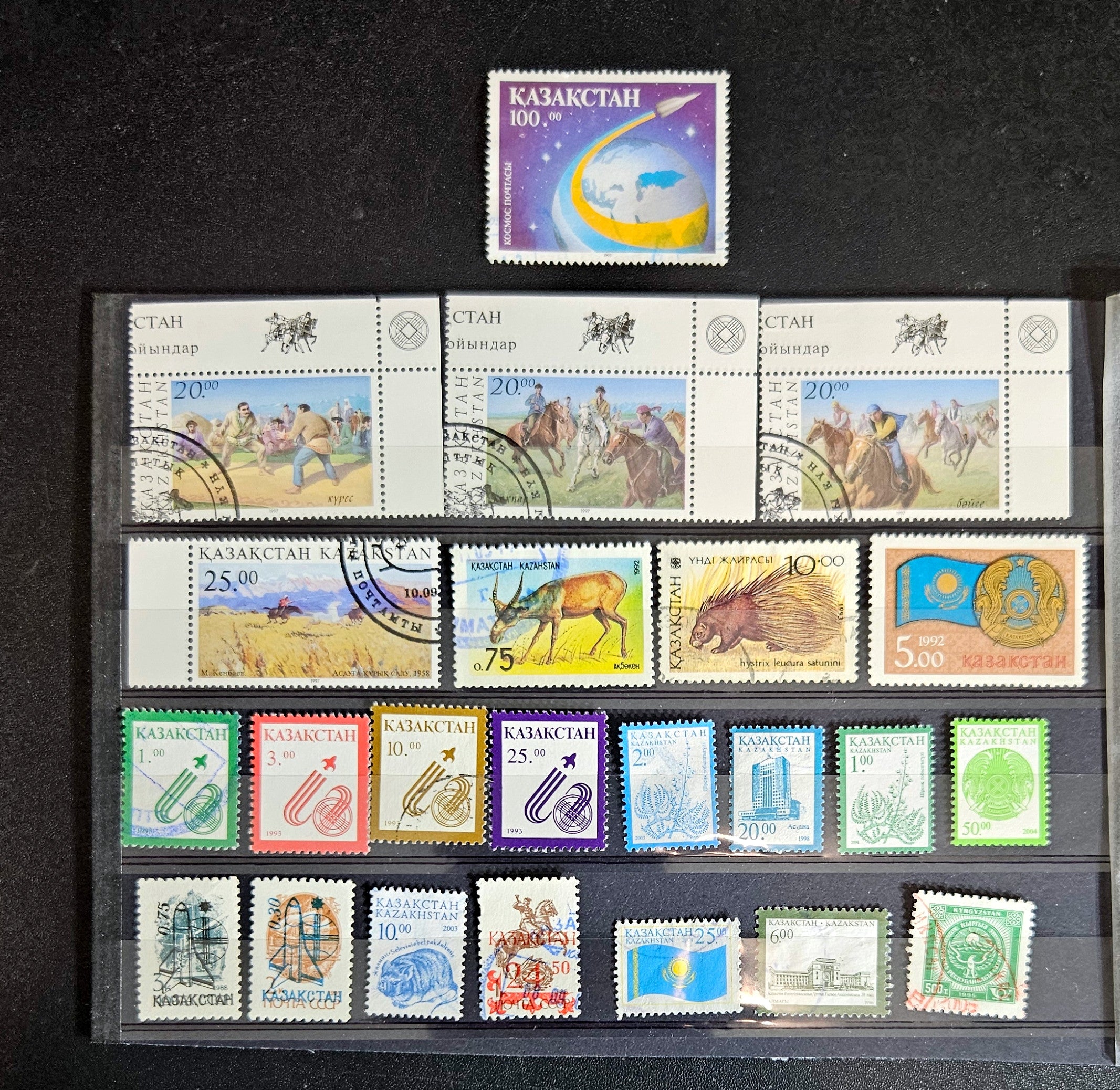 A collection of various Kazakhstan postage stamps displayed in a row, showcasing different designs and colors.