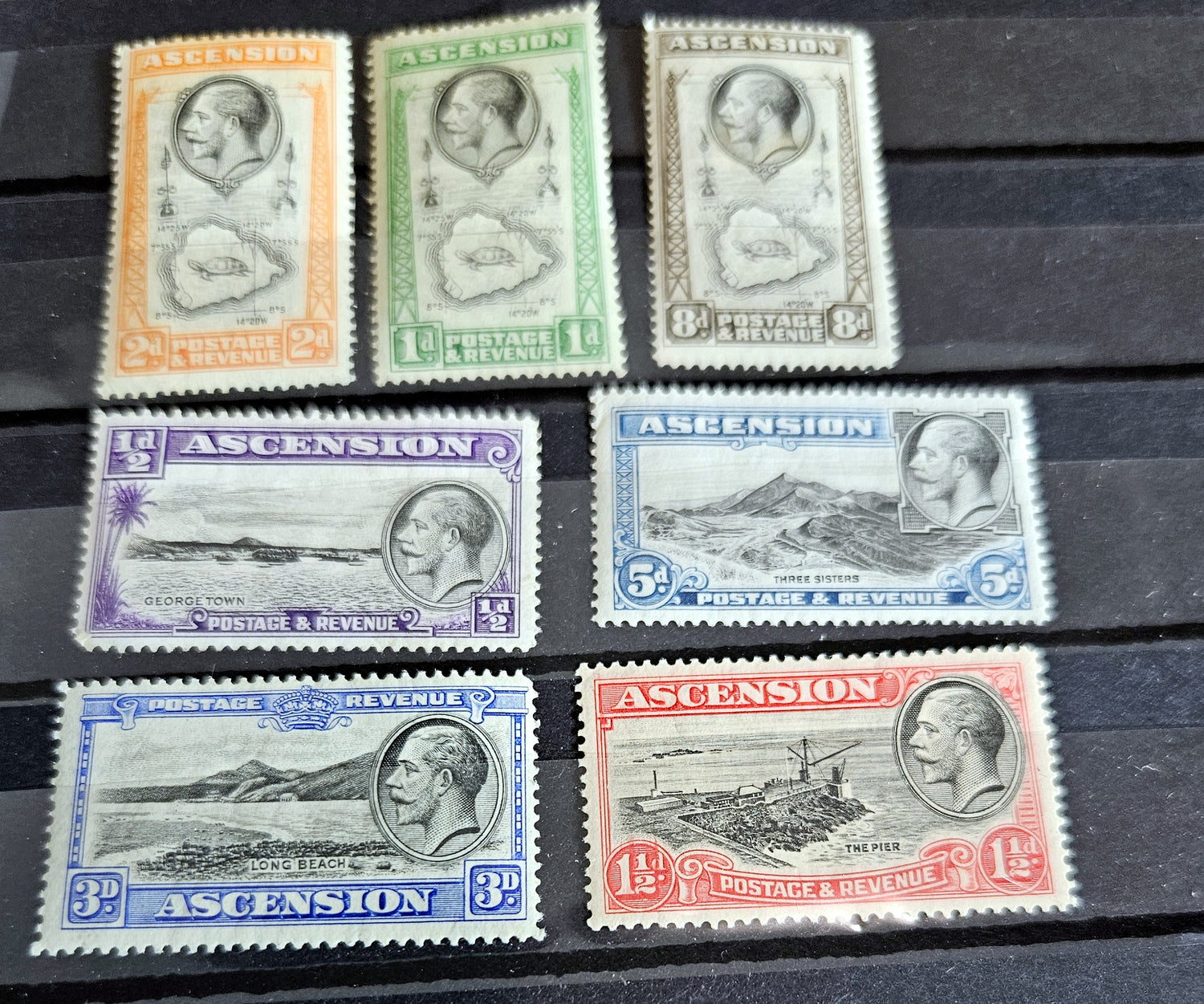 A collection of British Commonwealth Ascension vintage stamps displayed on a surface, featuring various colors and images representing different historical periods.