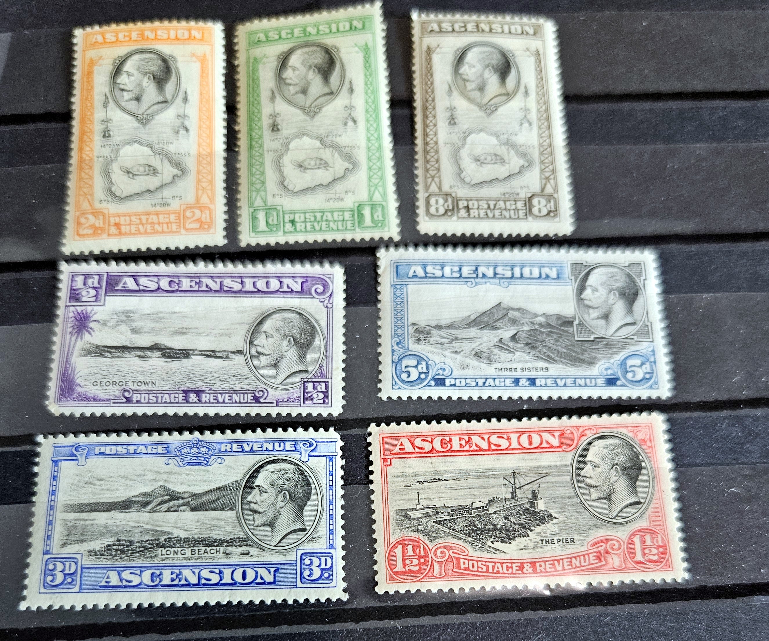 A collection of British Commonwealth Ascension vintage stamps displayed on a surface, featuring various colors and images representing different historical periods.