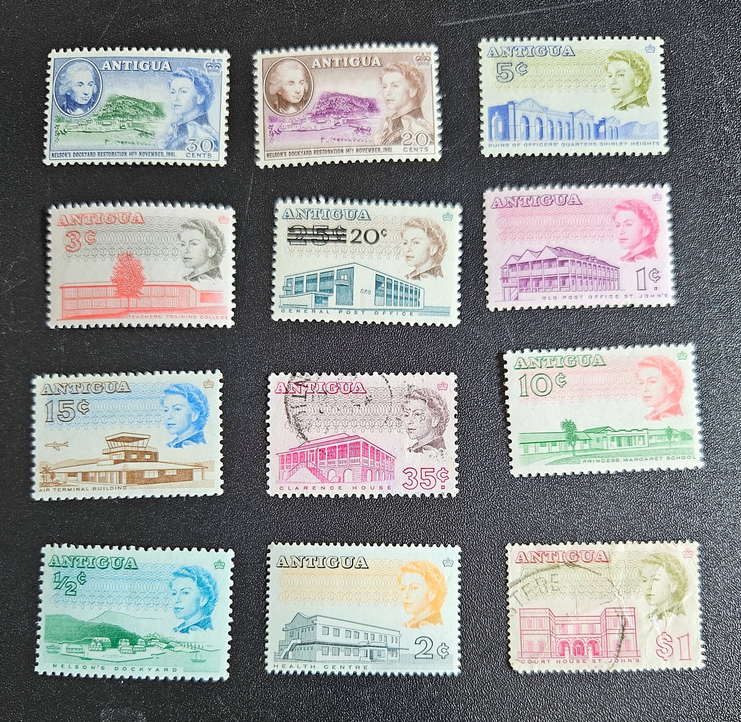 A collection of vintage Antigua postage stamps from the British Commonwealth, featuring various colors and designs, some depicting Queen Elizabeth II and others with scenic views.