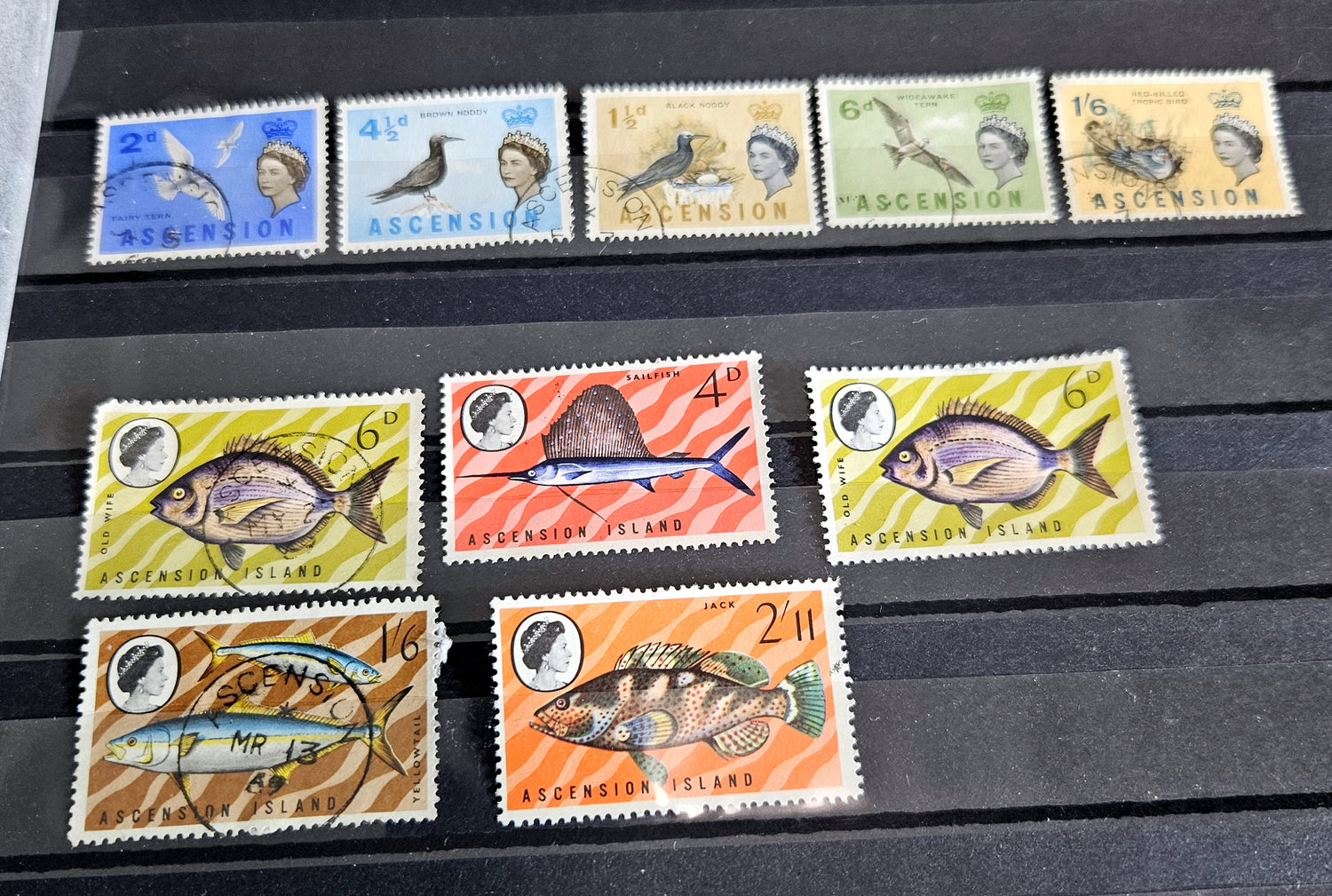 A collection of British Commonwealth Ascension vintage stamps displayed on a surface, featuring various colors and images representing different historical periods.