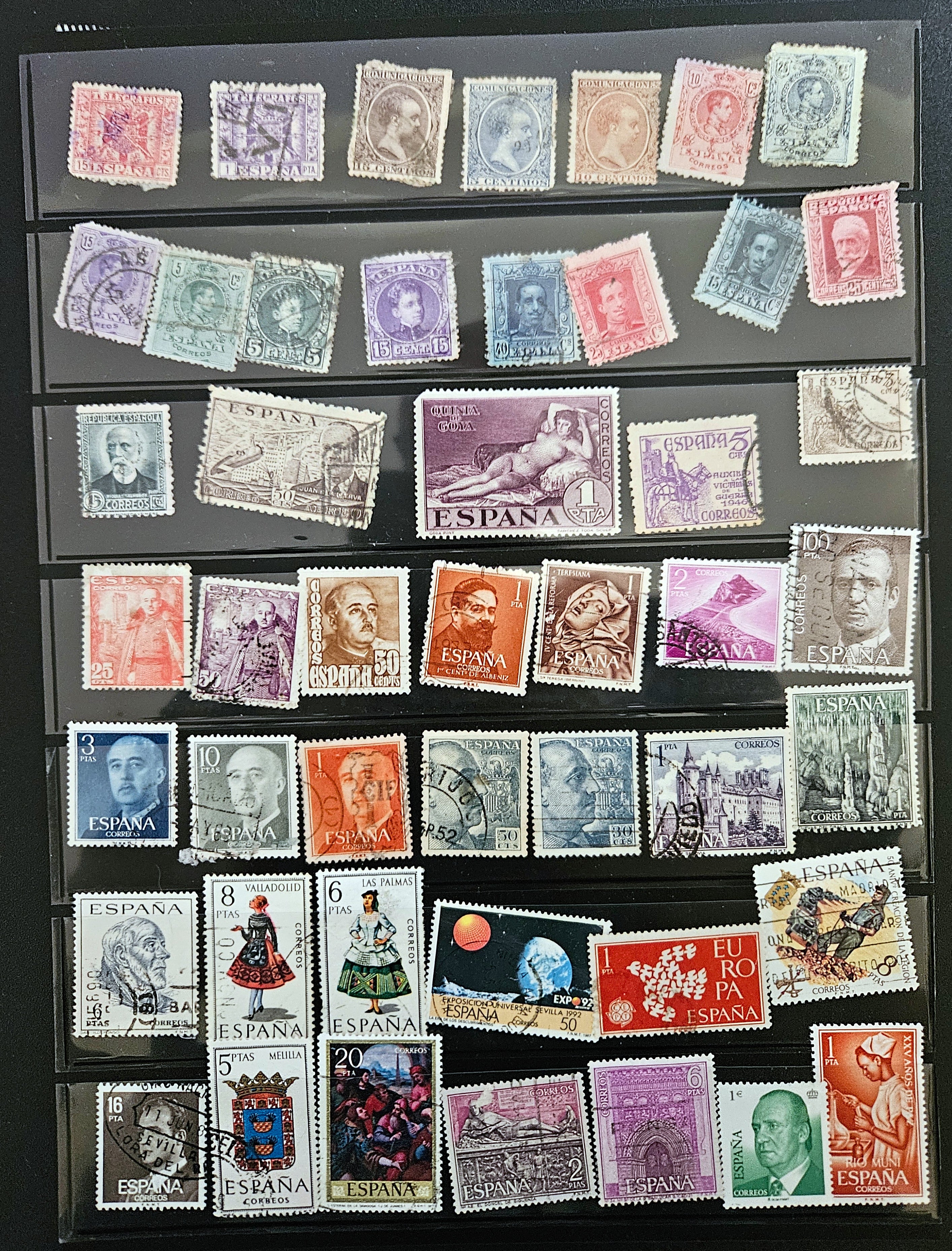 A display case filled with a variety of Spanish vintage postage stamps, featuring various colors and designs, arranged in rows.