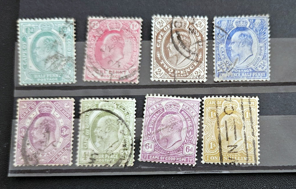 A set of eight vintage British postage stamps displayed on a clear plastic protector over a black background. The stamps feature various colors including blue, pink, brown, green, and yellow, with some showing cancellation marks.