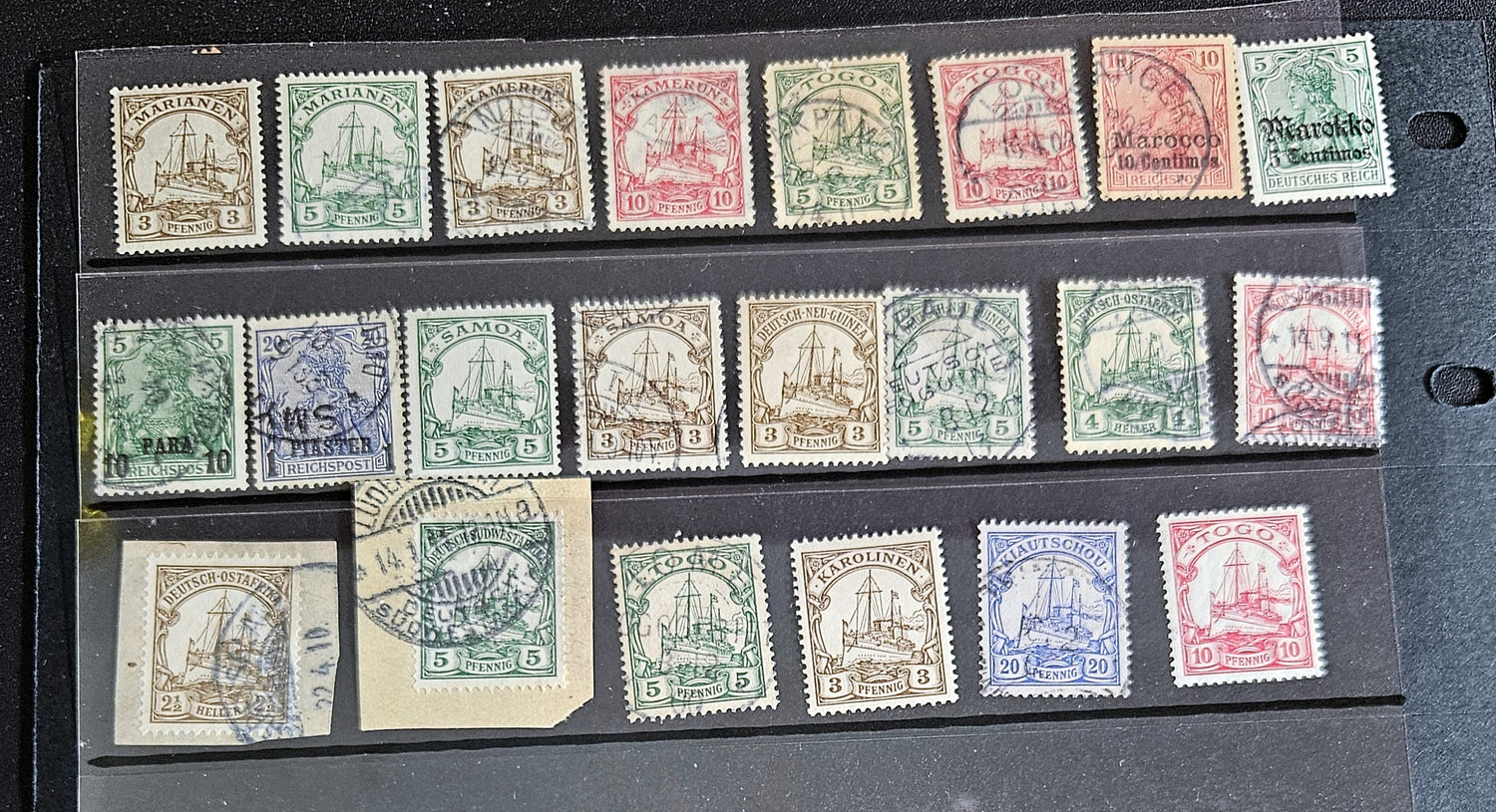A collection of vintage postage stamps from various German colonies, featuring different colors and designs, arranged in a row on a white background.