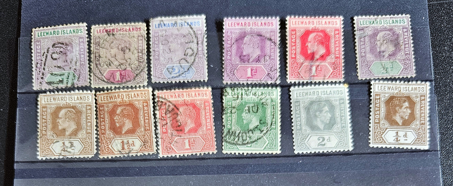 A collection of vintage Leeward Islands stamps featuring various monarchs from Queen Victoria to Queen Elizabeth II, displayed on a flat surface.