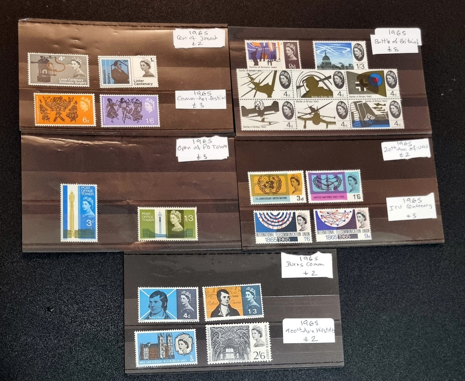 A collection of various commemorative postage stamps featuring Queen Elizabeth II, arranged in a clear plastic case with descriptive labels.