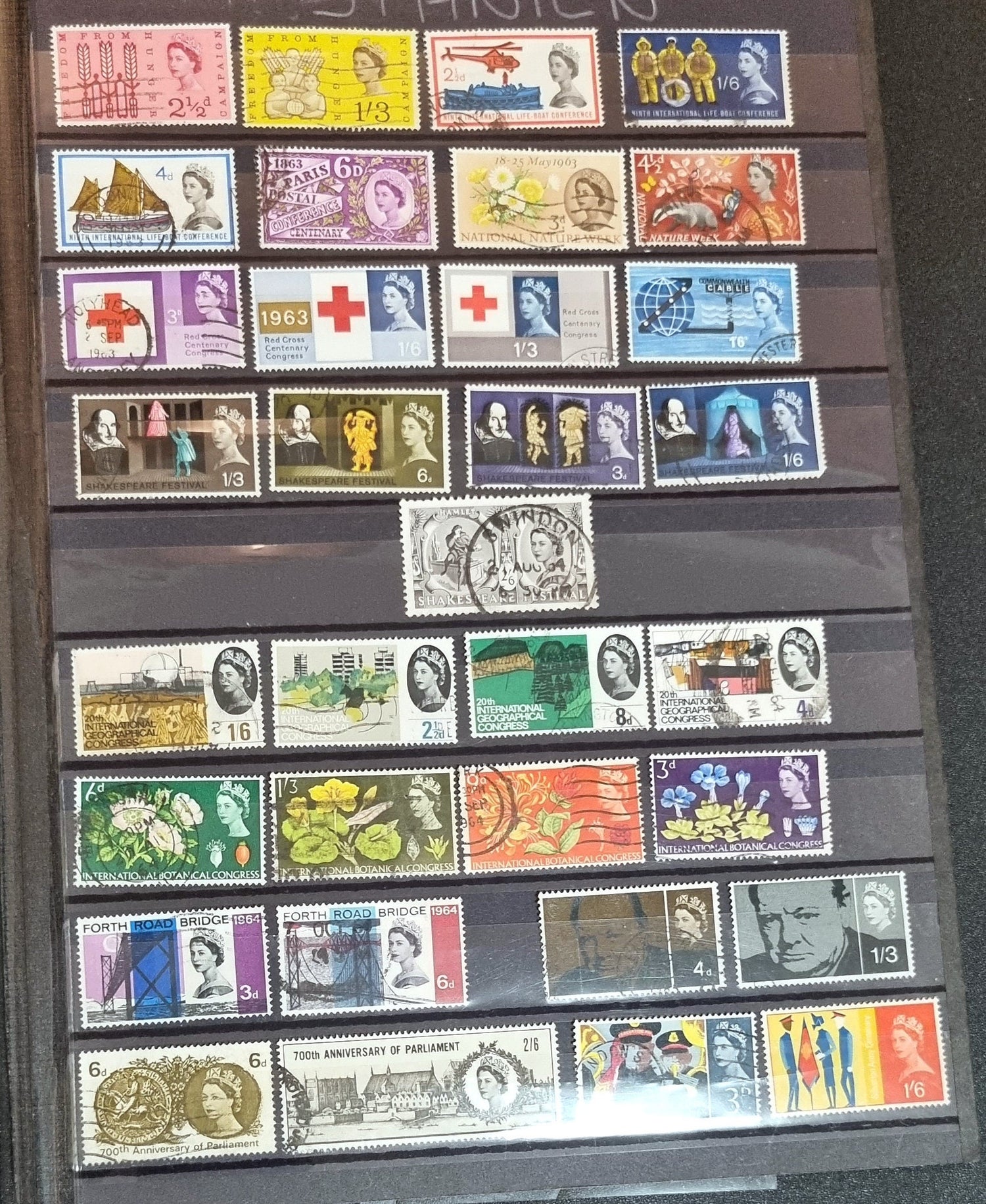 A collection of various commemorative postage stamps featuring Queen Elizabeth II, arranged in a clear plastic case with descriptive labels.