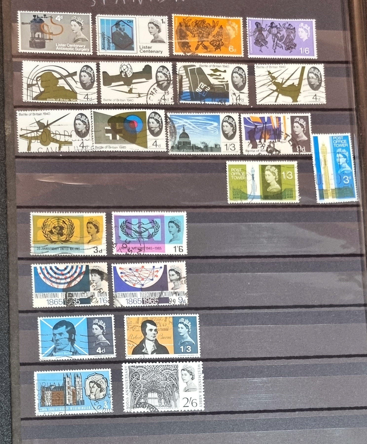A collection of various commemorative postage stamps featuring Queen Elizabeth II, arranged in a clear plastic case with descriptive labels.