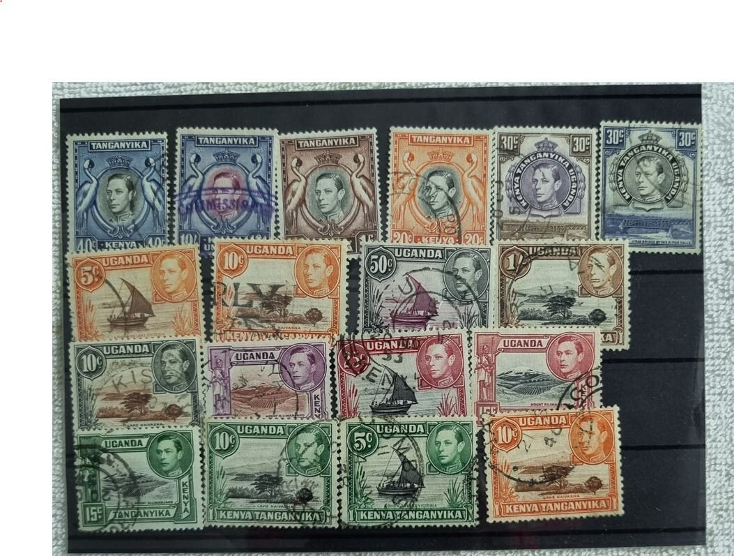 A display of various postage stamps from Kenya, Uganda, and Tanganyika featuring portraits of King George V, King George VI, and Queen Elizabeth II.