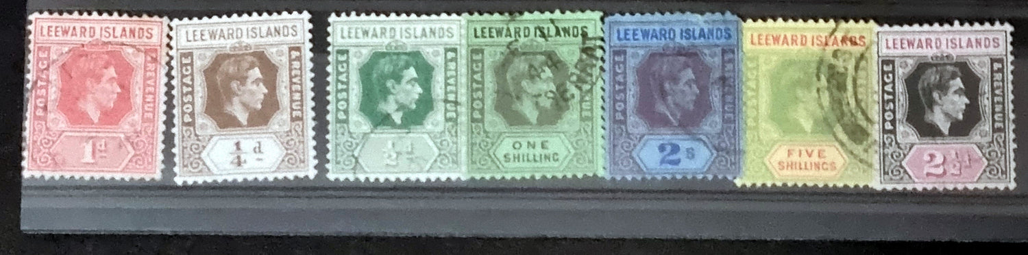 A collection of vintage Leeward Islands stamps featuring various monarchs from Queen Victoria to Queen Elizabeth II, displayed on a flat surface.