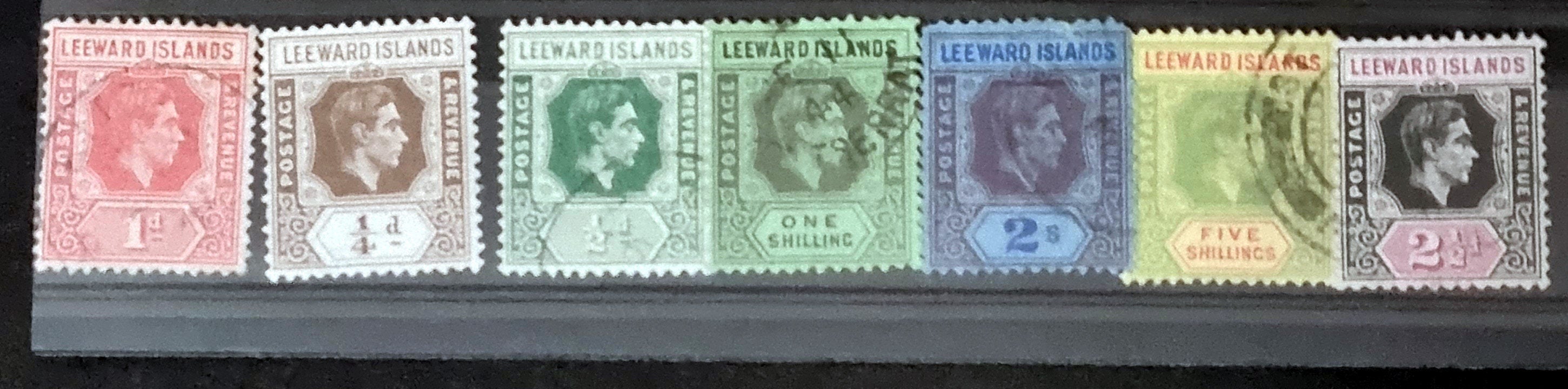 A collection of vintage Leeward Islands stamps featuring various monarchs from Queen Victoria to Queen Elizabeth II, displayed on a flat surface.
