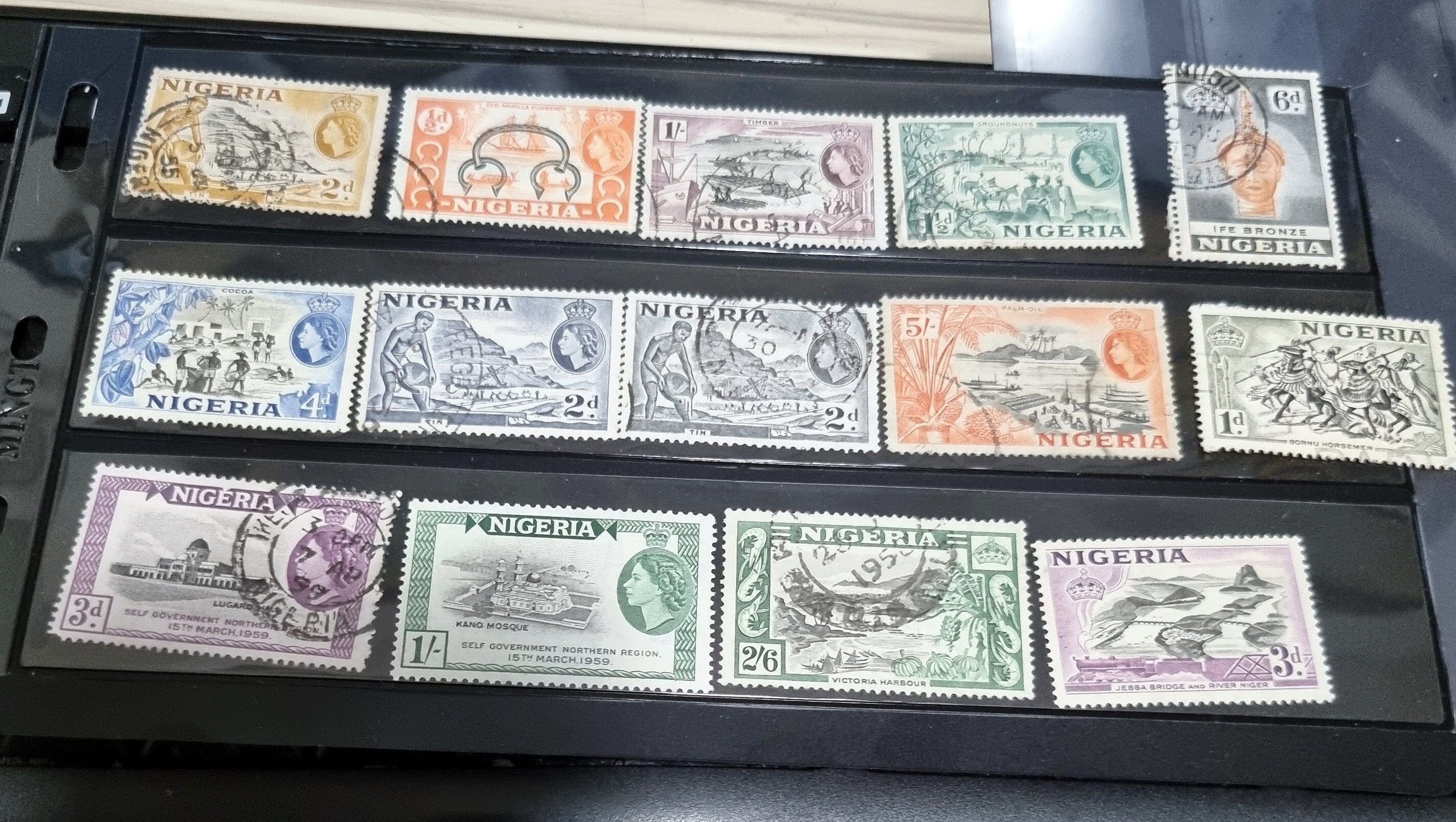 A collection of vintage British Nigeria stamps displayed on a surface, featuring various colors and motifs related to different eras in Nigerian history.