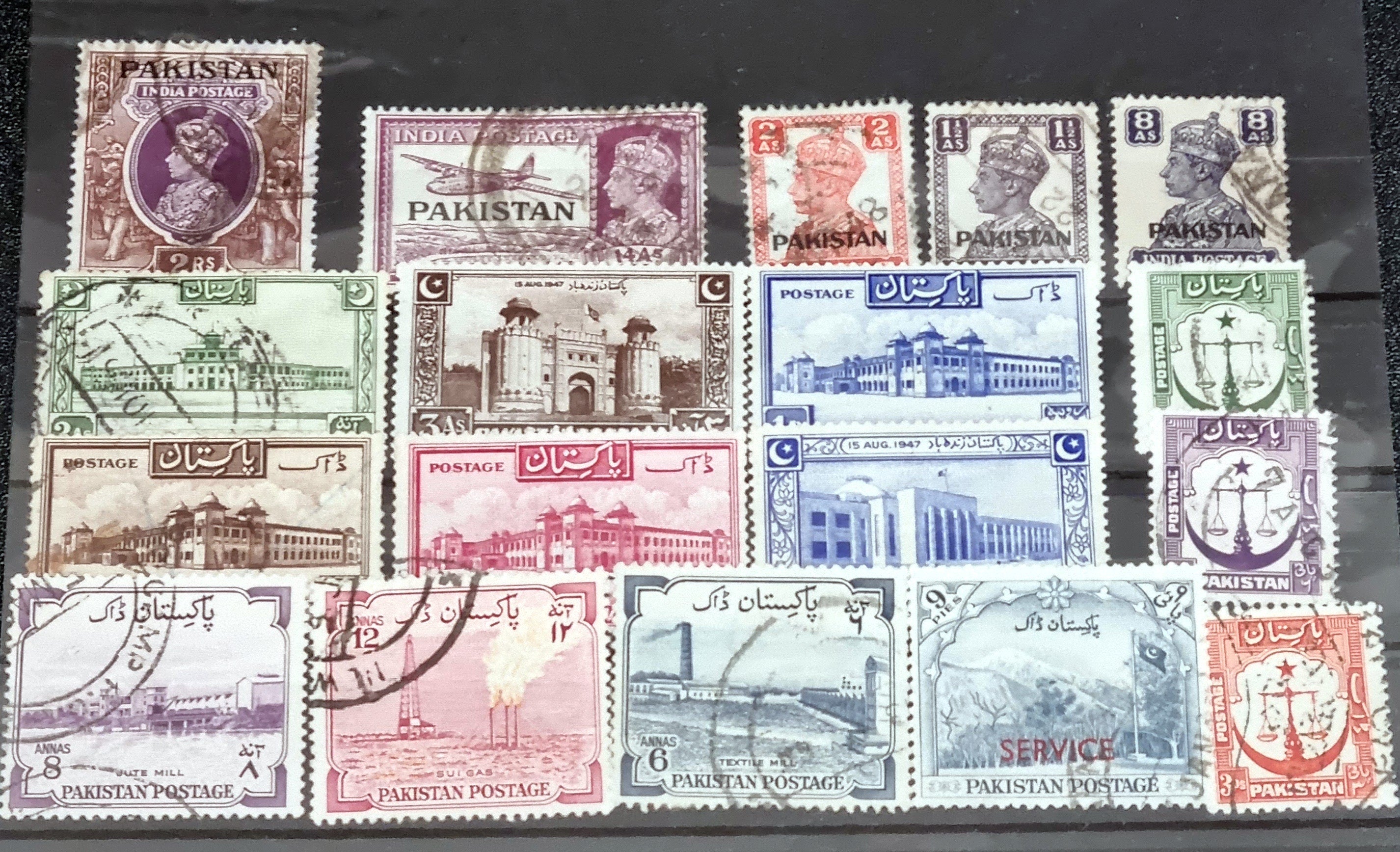 A collection of vintage Pakistan stamps from various periods, showing different designs and denominations, displayed on a glass surface.