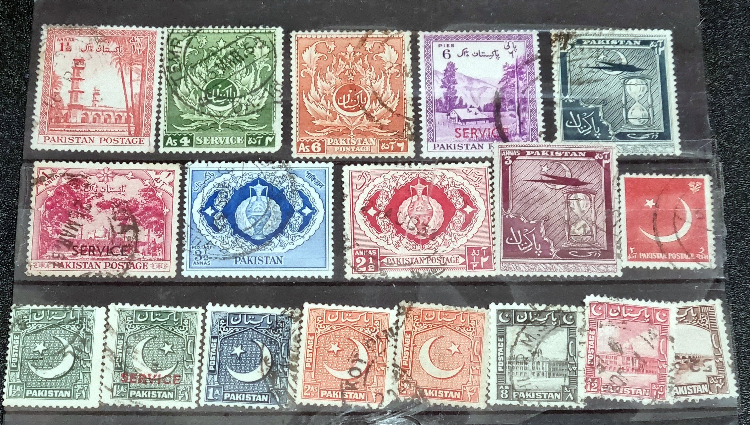 A collection of vintage Pakistan stamps from various periods, showing different designs and denominations, displayed on a glass surface.
