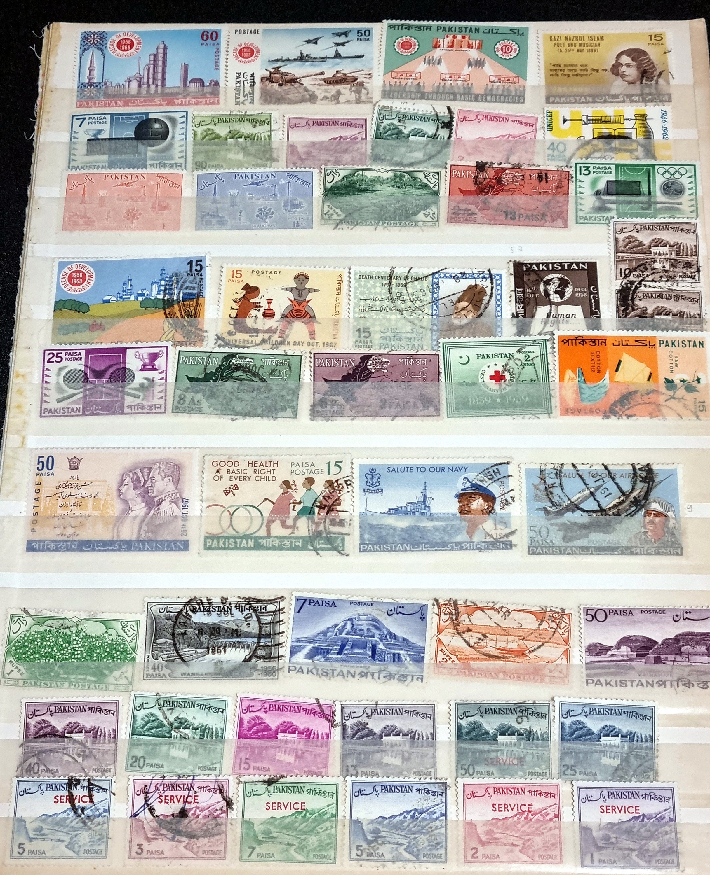 A collection of vintage Pakistan stamps from various periods, showing different designs and denominations, displayed on a glass surface.