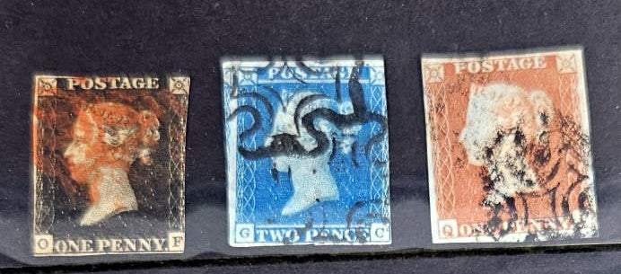 Three vintage British postage stamps displayed side by side on a dark background: a brown one penny stamp with Queen Victoria&
