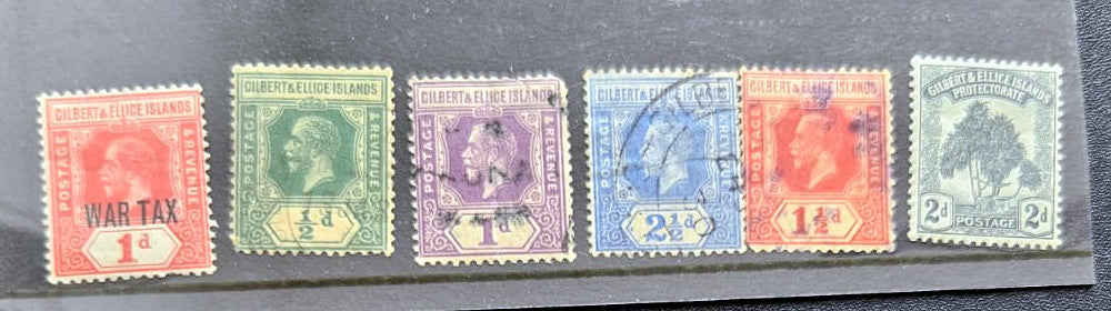 Six vintage postage stamps from the British Gilbert, displayed side-by-side on a dark background. The stamps feature various colors including red, green, purple, blue, orange, and gray, with some showing cancellation marks.