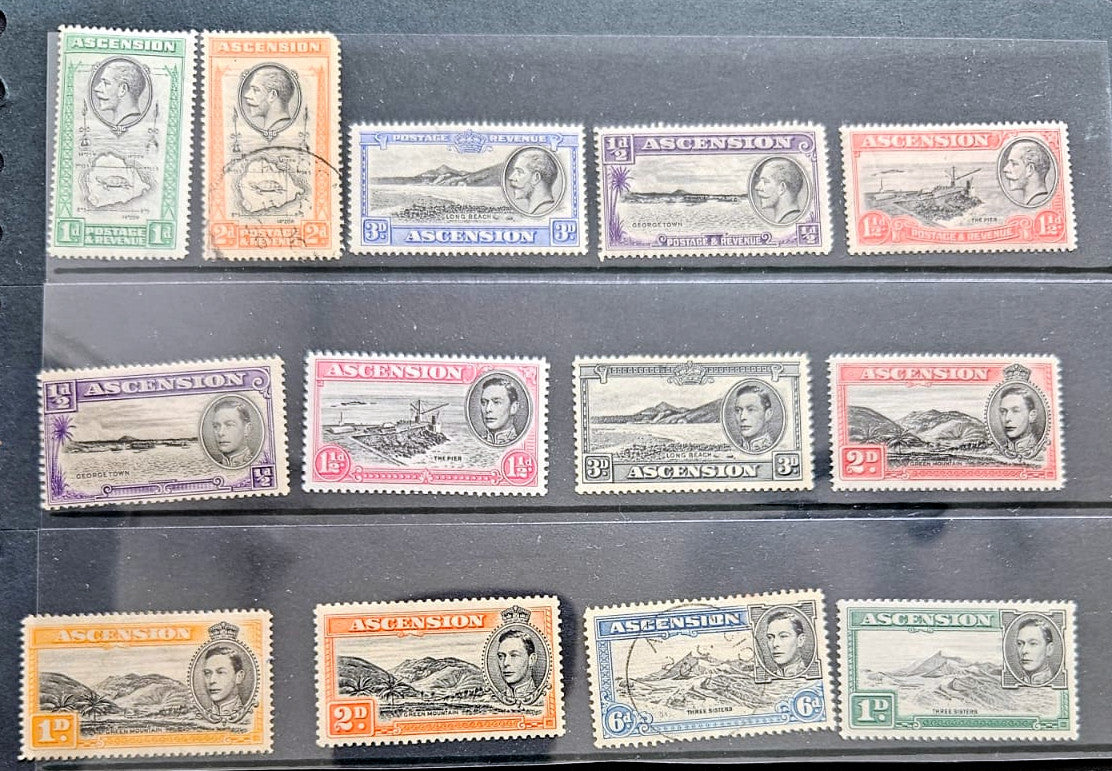 A set of vintage Ascension Island postage stamps arranged in three rows on a dark background. The stamps feature various colors including green, orange, blue, purple, and red, with some showing portrait illustrations and others depicting landscapes.