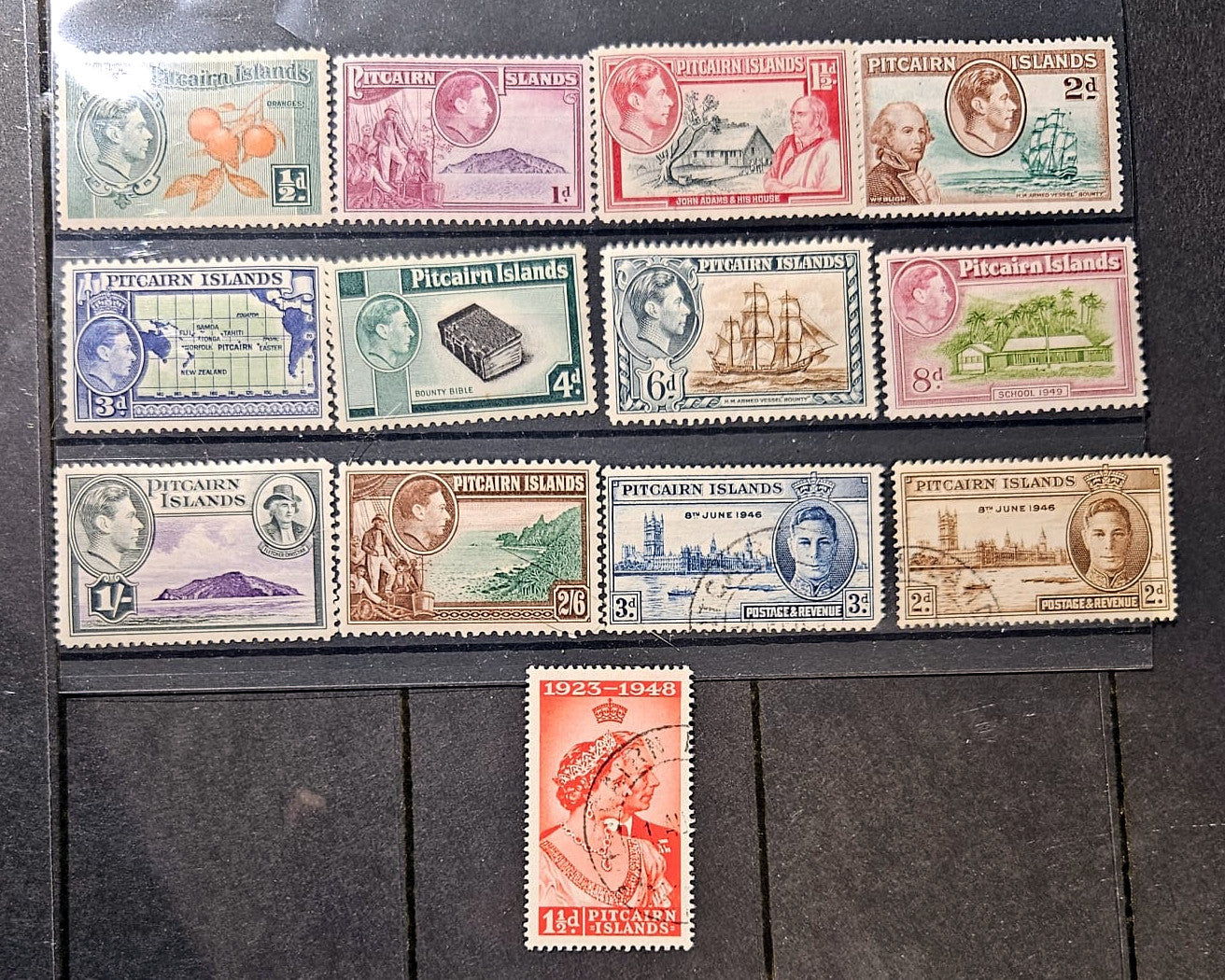 A collection of vintage Pitcairn Islands postage stamps arranged on a dark wooden surface, with a single red stamp placed below the group.