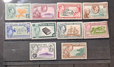 A set of vintage Pitcairn Islands postage stamps arranged on a dark wooden surface. The stamps feature various colors and designs, including portraits of King George V, landscapes, ships, and postal illustrations, with denominations ranging from 1d to 26d.