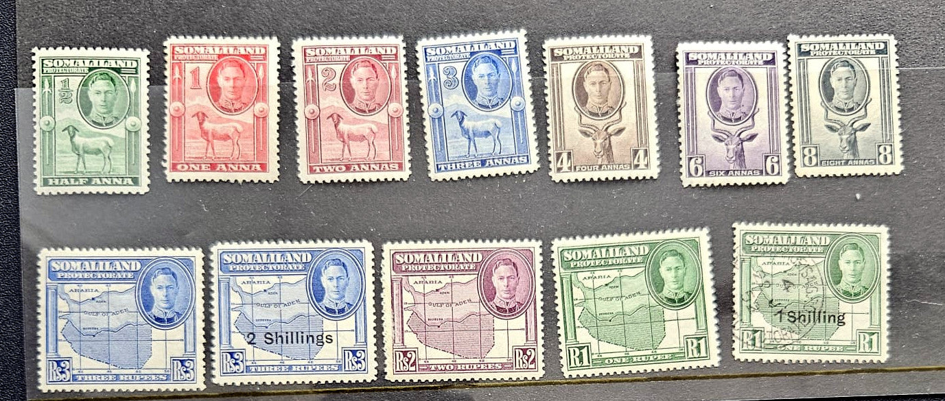 A set of vintage Somali postage stamps arranged in two rows on a dark background. The top row contains seven stamps in green, red, blue, tan, purple, and lavender shades, while the bottom row contains six additional stamps in blue, tan, green, and lavender tones.