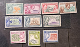 A set of ten vintage Pitcairn Islands postage stamps from 1956, displayed on a dark textured background. The stamps feature various colors including green, pink, red, blue, and yellow, with designs depicting local landmarks, flora, and fauna.