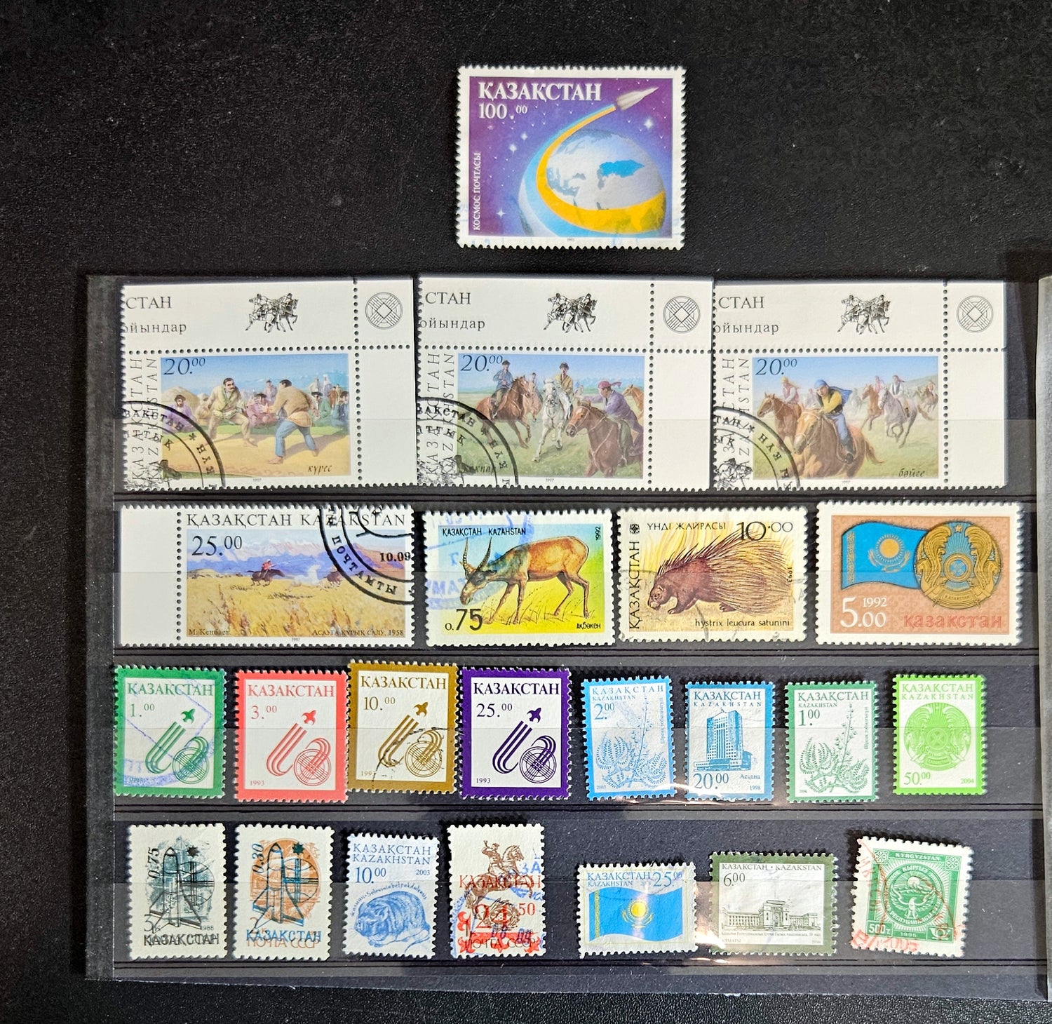 A collection of various Kazakhstan postage stamps displayed in a row, showcasing different designs and colors.