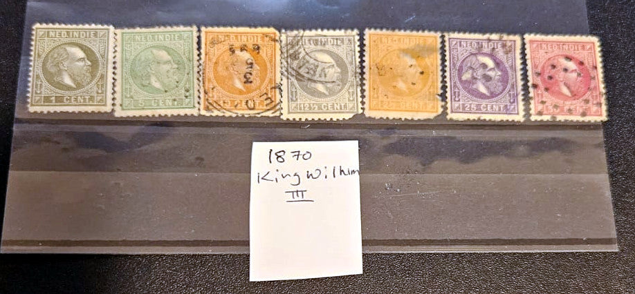 A set of eight vintage British Colonies 1870 King William III postage stamps displayed in a clear plastic case, with a handwritten white label in front.