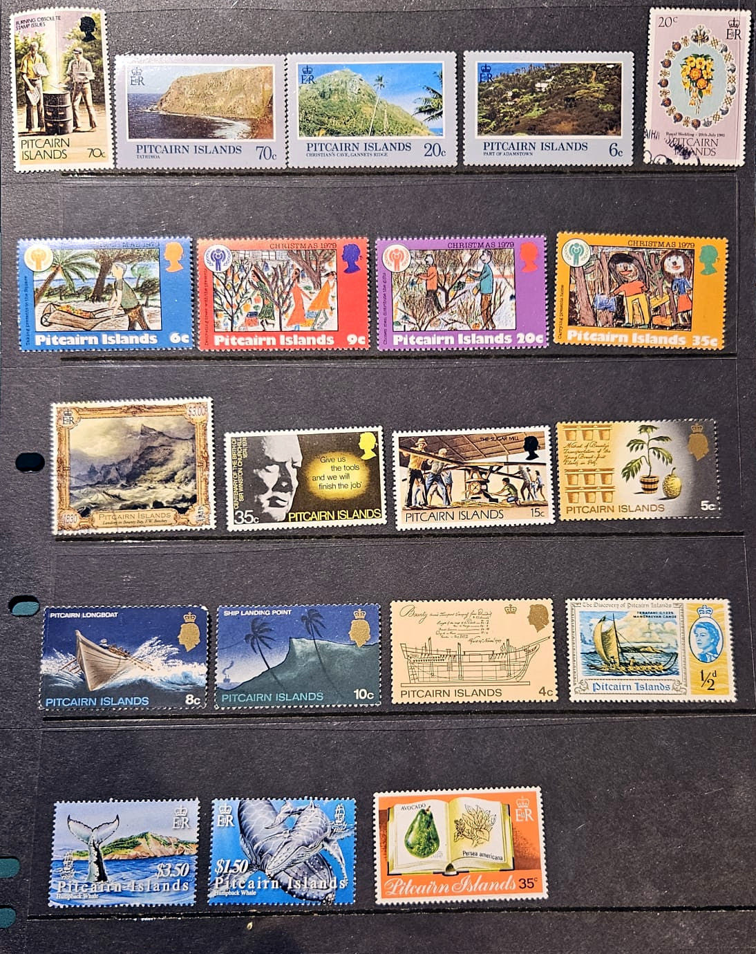 A collection of vintage Pitcairn Islands postage stamps arranged on a black display card, showing various landscapes, figures, and scenes with different colors and denominations.