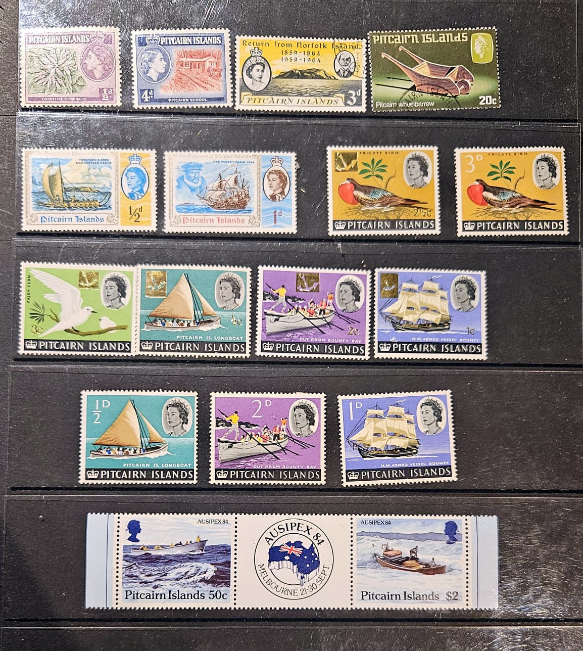 A collection of vintage Pitcairn Islands postage stamps arranged on a dark wooden surface, including various single stamp pieces and a horizontal strip of stamps.