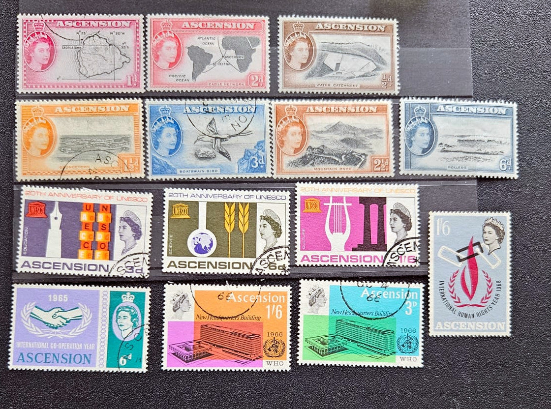 A set of twelve vintage Ascension postage stamps from Sierra Leone, arranged in three rows on a dark textured background. The stamps feature various colors and designs, including portraits of Queen Elizabeth II, maps, and industrial motifs.