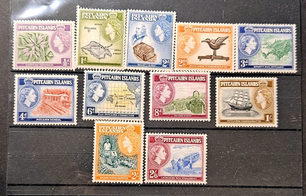 A set of vintage Pitcairn Islands postage stamps displayed on a dark wooden surface. The collection includes stamps in various colors (purple, green, blue, orange, brown, red) featuring different illustrations and denominations.