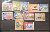 A set of vintage Pitcairn Islands postage stamps displayed on a dark wooden surface. The collection includes stamps in various colors (purple, green, blue, orange, brown, red) featuring different illustrations and denominations.