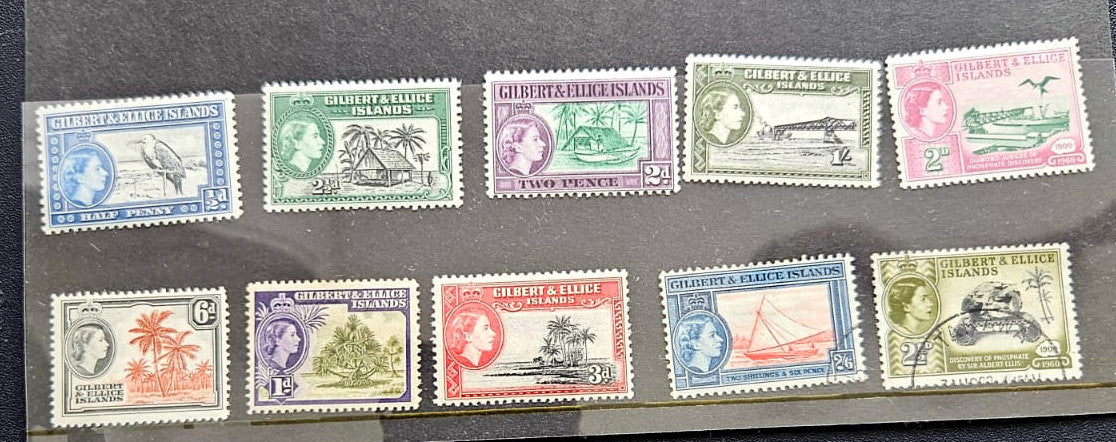 A set of twelve vintage Gilbert postage stamps displayed on a dark gray background, featuring various colors and designs from 1956.