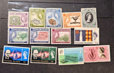 A set of vintage Pitcairn Islands postage stamps arranged on a dark wooden surface. The stamps feature various designs, including Queen Elizabeth II portraits, landscapes, and architectural scenes, with different colors and denominations.