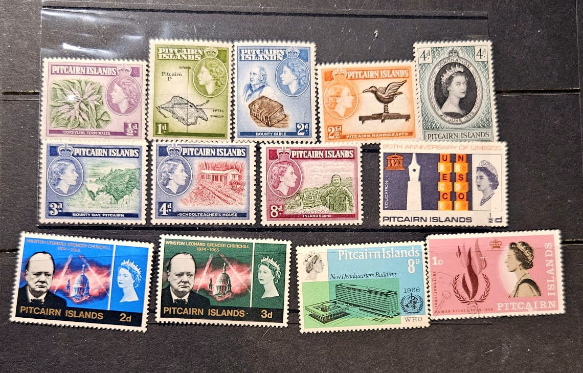 A set of vintage Pitcairn Islands postage stamps arranged on a dark wooden surface. The stamps feature various designs, including Queen Elizabeth II portraits, landscapes, and architectural scenes, with different colors and denominations.
