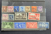 A collection of vintage British and Commonwealth postage stamps displayed on a clear plastic holder against a dark textured background. The stamps feature various colors including blue, red, green, orange, purple, and brown, with Queen Elizabeth II portraits.