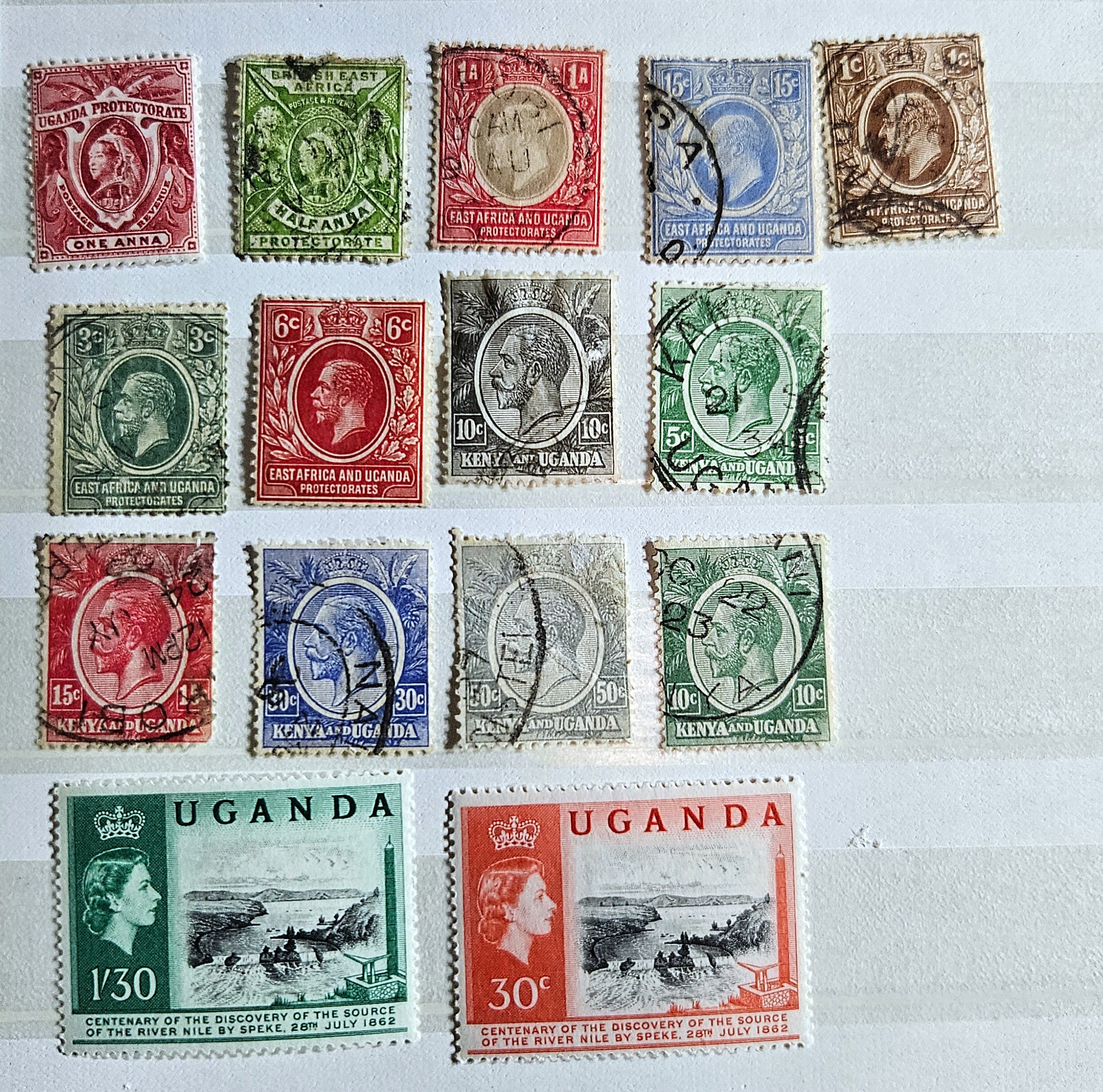 A collection of British Commonwealth Uganda stamps from various monarchs displayed on a surface.