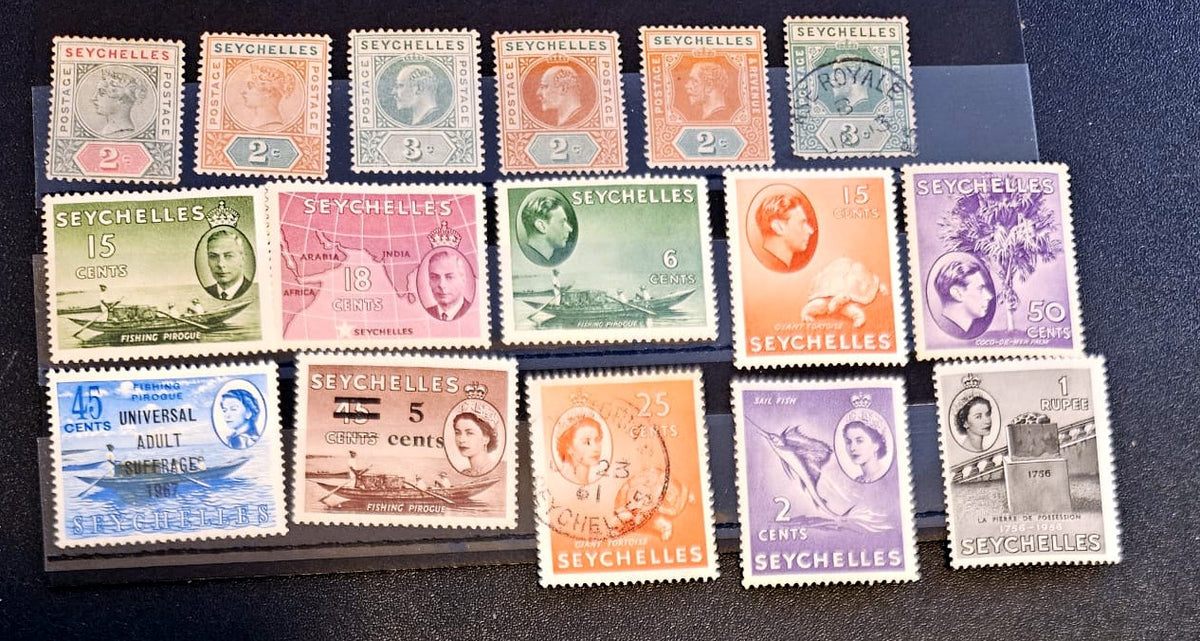 A collection of vintage Seychelles postage stamps arranged on a black surface, showing multiple denominations and colors including green, orange, purple, blue, and red.