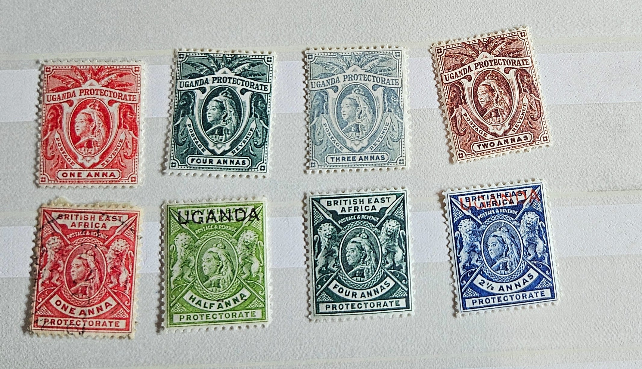 A collection of British Commonwealth Uganda stamps from various monarchs displayed on a surface.