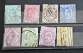 A set of eight vintage British postage stamps displayed on a clear plastic protector over a black background. The stamps feature various colors including blue, pink, brown, green, and yellow, with some showing cancellation marks.
