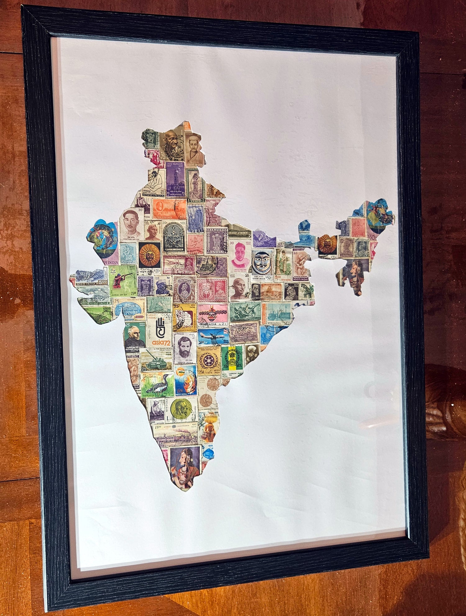 Framed artwork of a map of India made from postage stamps on a wooden surface.