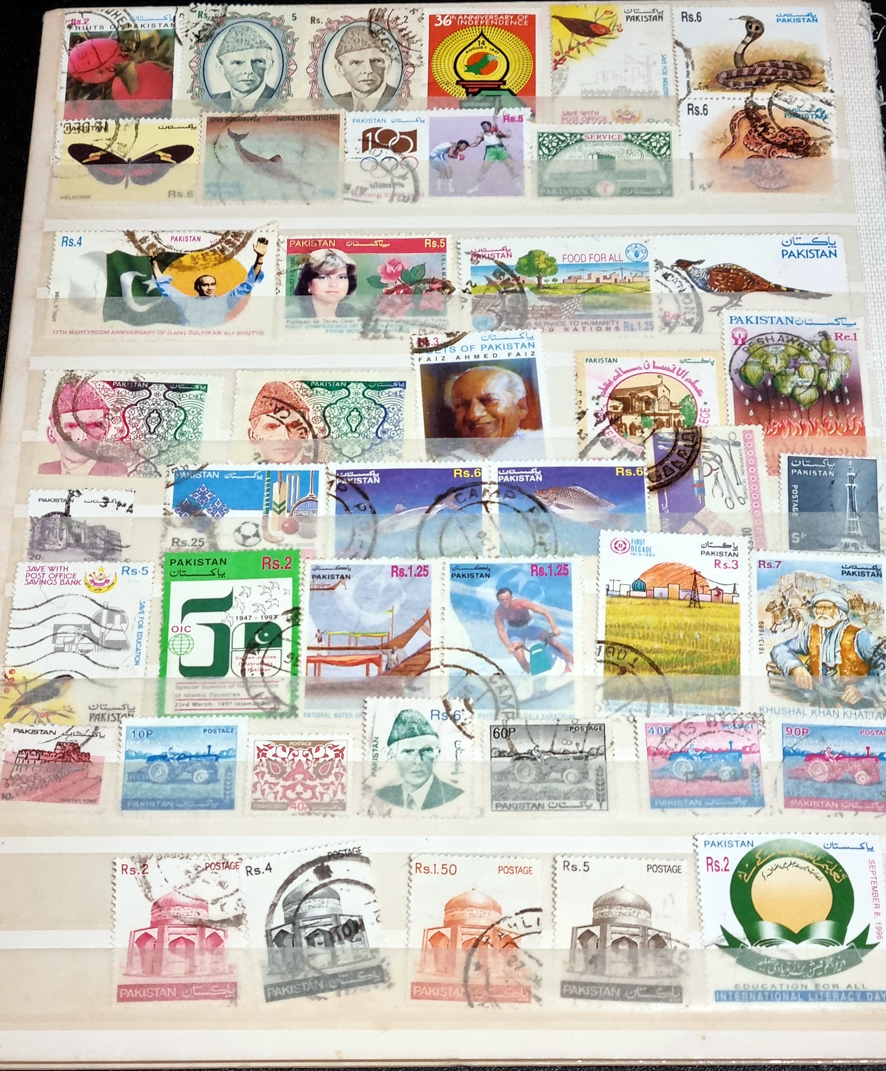 A collection of vintage Pakistan stamps from various periods, showing different designs and denominations, displayed on a glass surface.