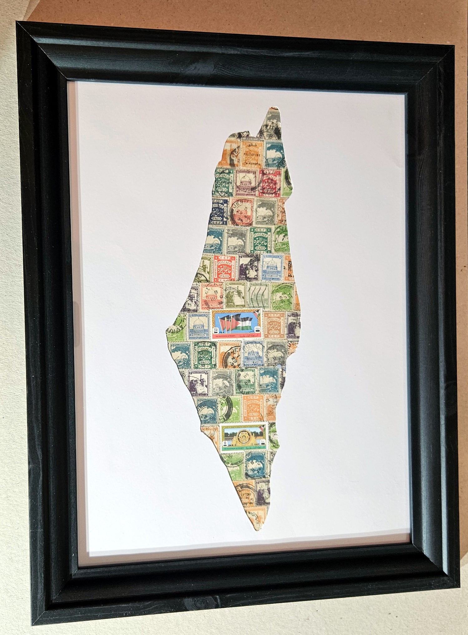 Framed artwork of a map of palestine made from vintage stamps on a white background.