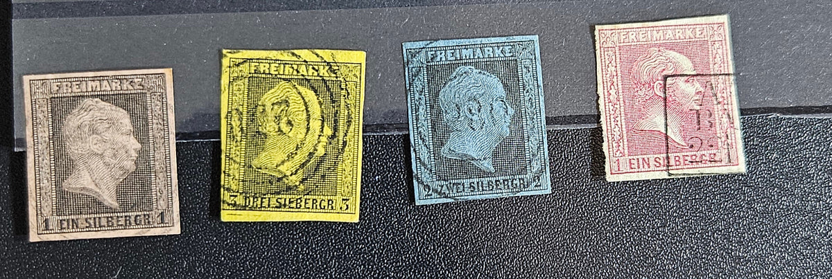 Four vintage Prussian postage stamps in different colors (gray, yellow, blue-gray, and pinkish-red) aligned horizontally on a black textured background.